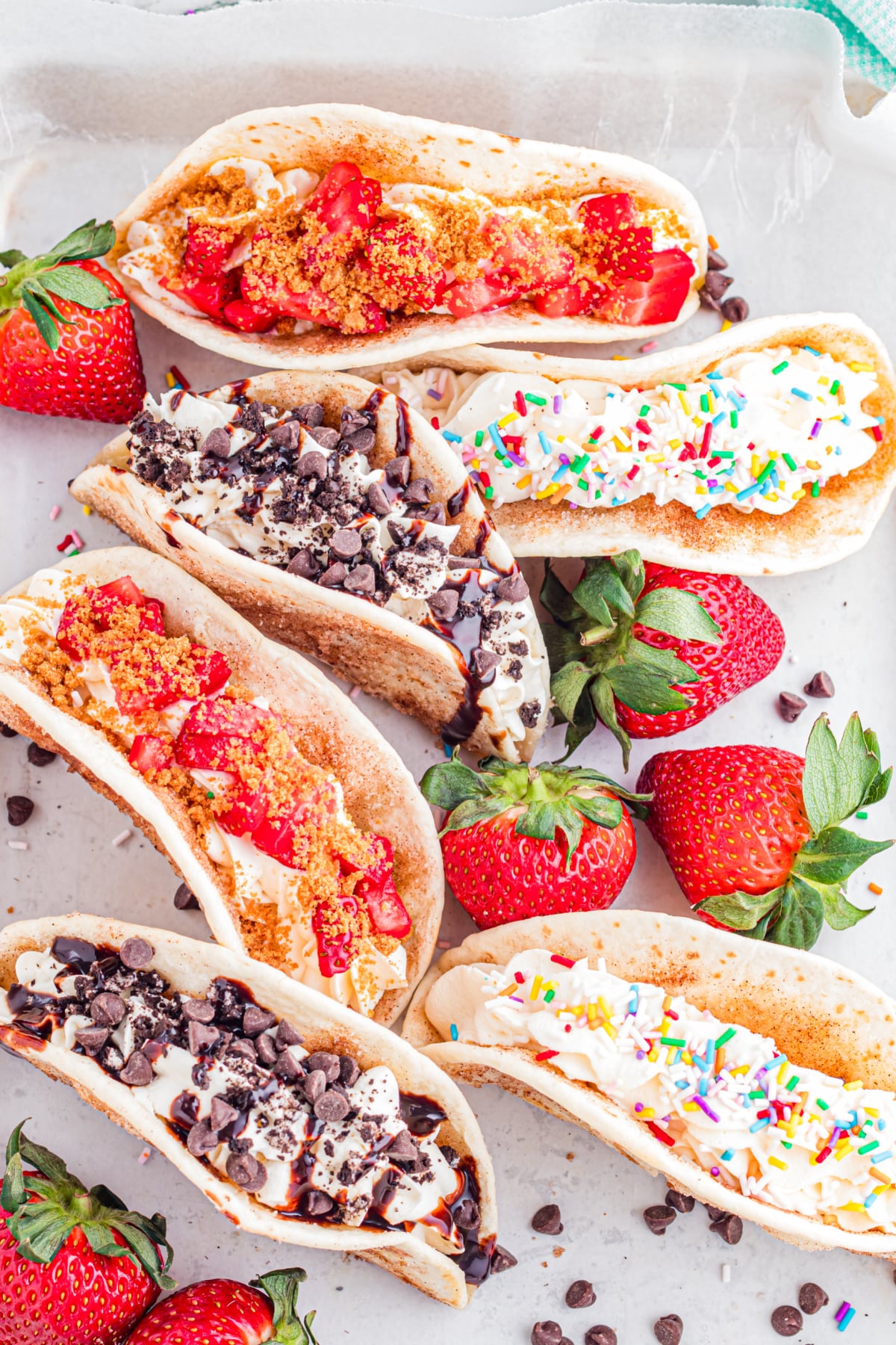 A bunch of dessert tacos with different toppings like chocolate chips, sprinkles and strawberries.