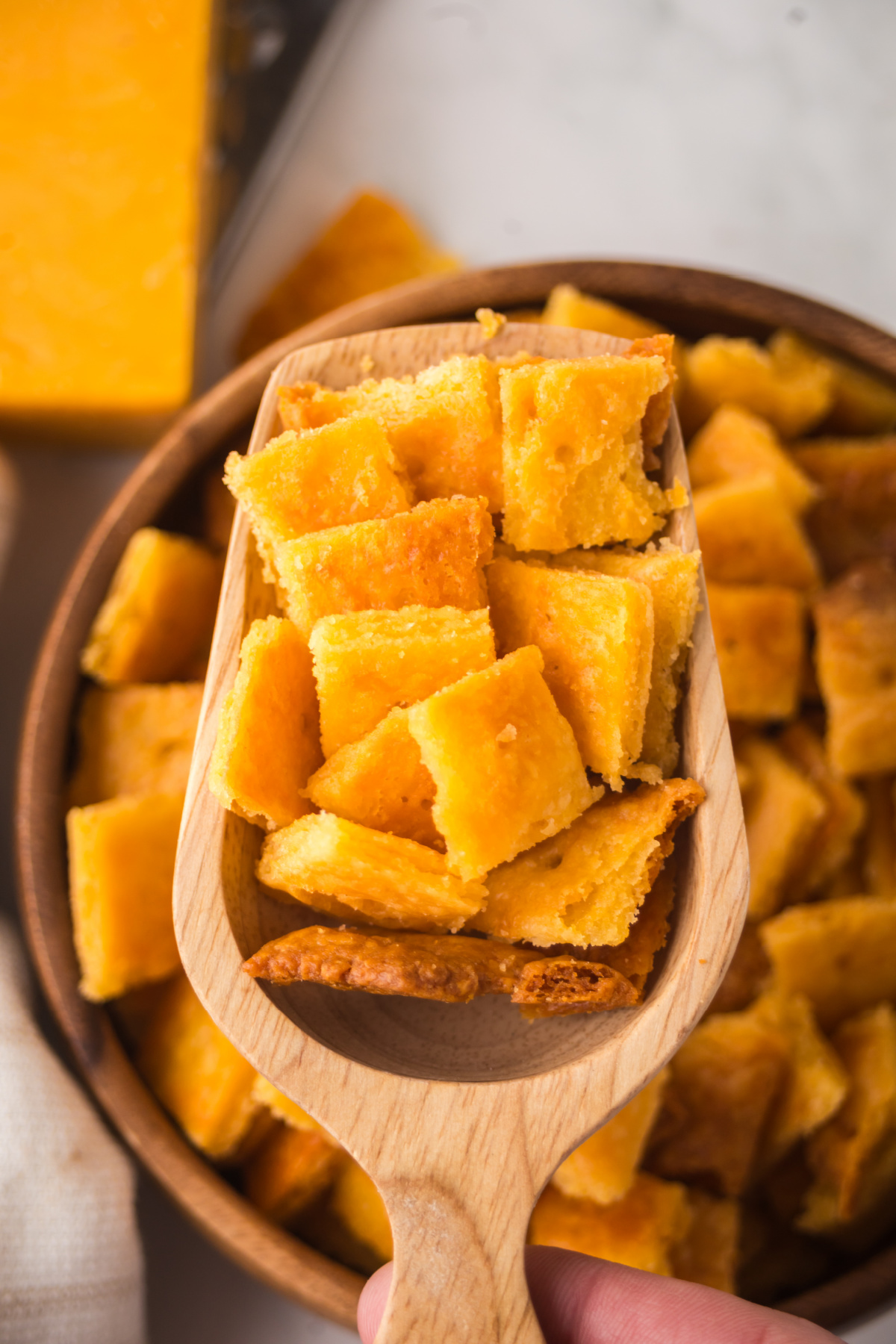 A wooden scoop serving cheez its from a wooden bowl.
