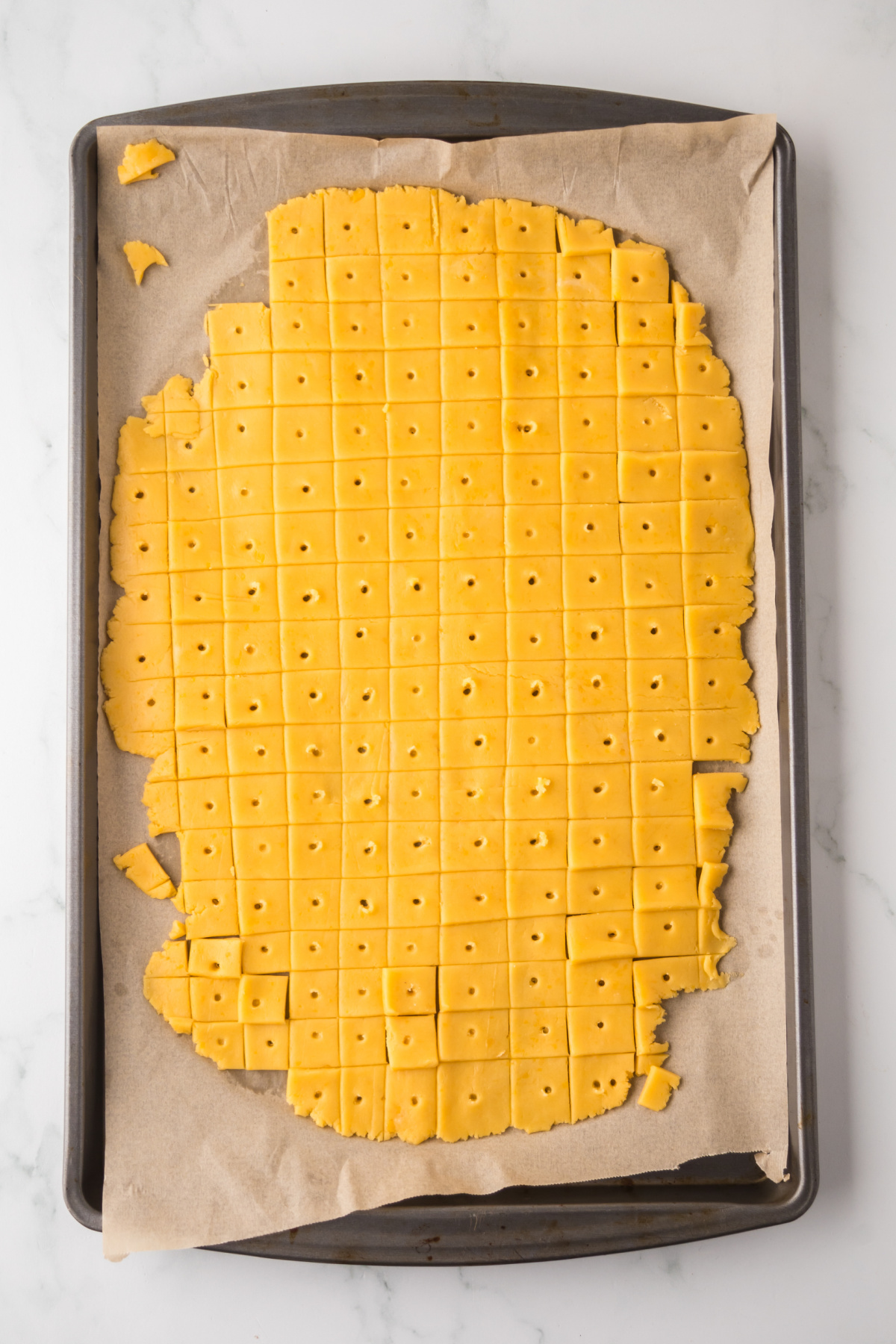 Dough rolled out on a parchment covered baking sheet cut into squares with a hole in the middle.