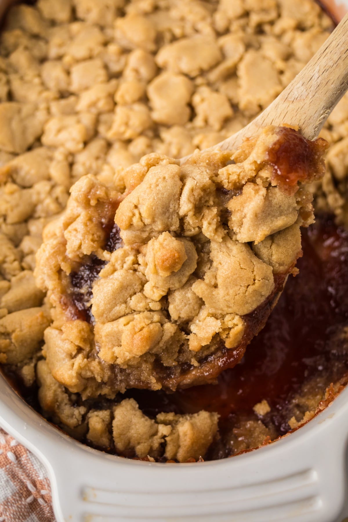 a wooden spoon lifting a serving out of the baking dish