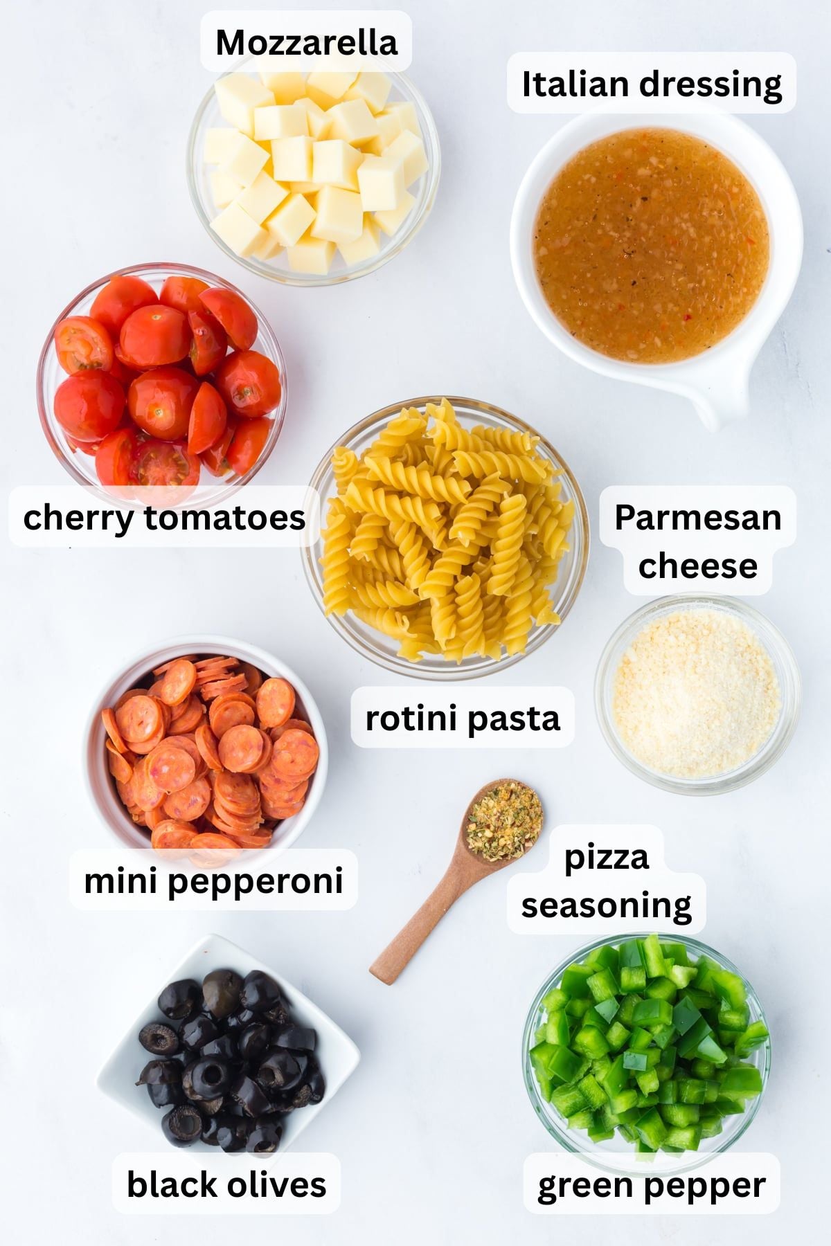 All the ingredients needed to make Pizza Pasta Salad in bowls on a table