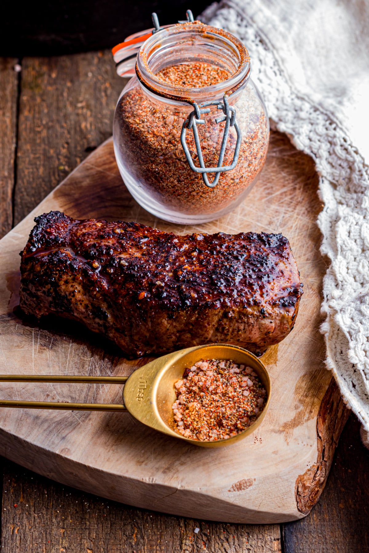 Glass jar full of seasoning, a cooked steak and a spoonful of seasoning on a cutting board.