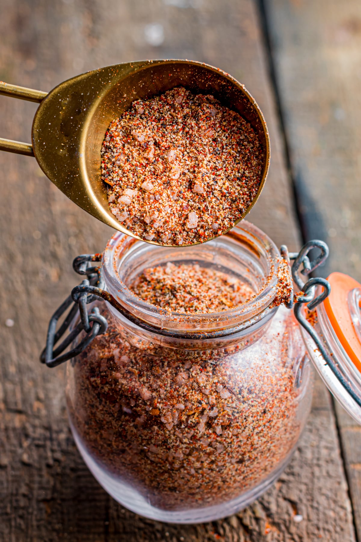 A spoon adding blended seasoning to a glass jar with an airtight lid.