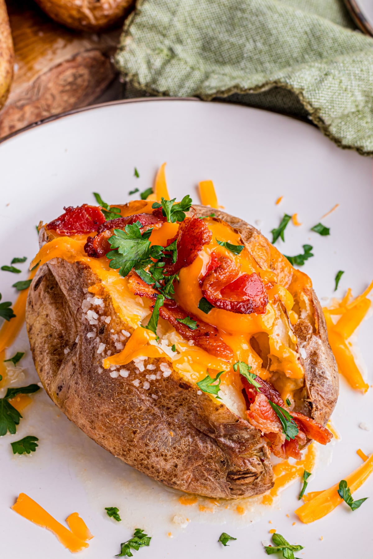 A baked-potato full of sour cream, chives, cheese, bacon on a plate.