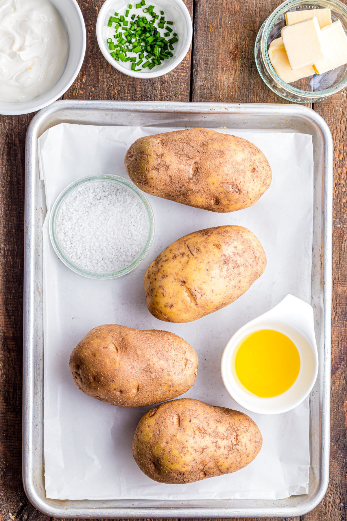 A parchment covered baking sheet with potatoes and a bowl of oil and salt.