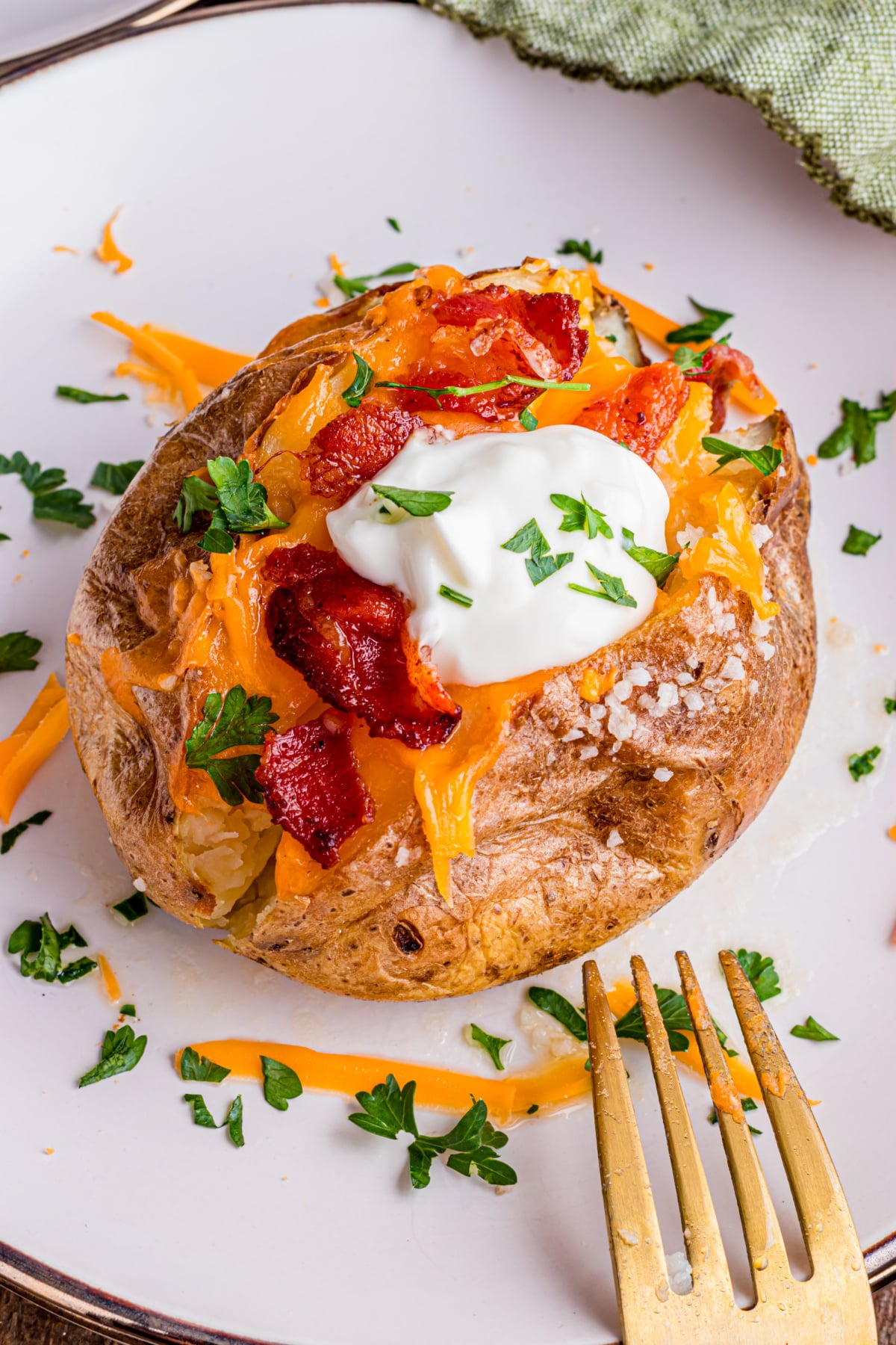 A baked-potato full of sour cream, chives, cheese, bacon on a plate with a fork.