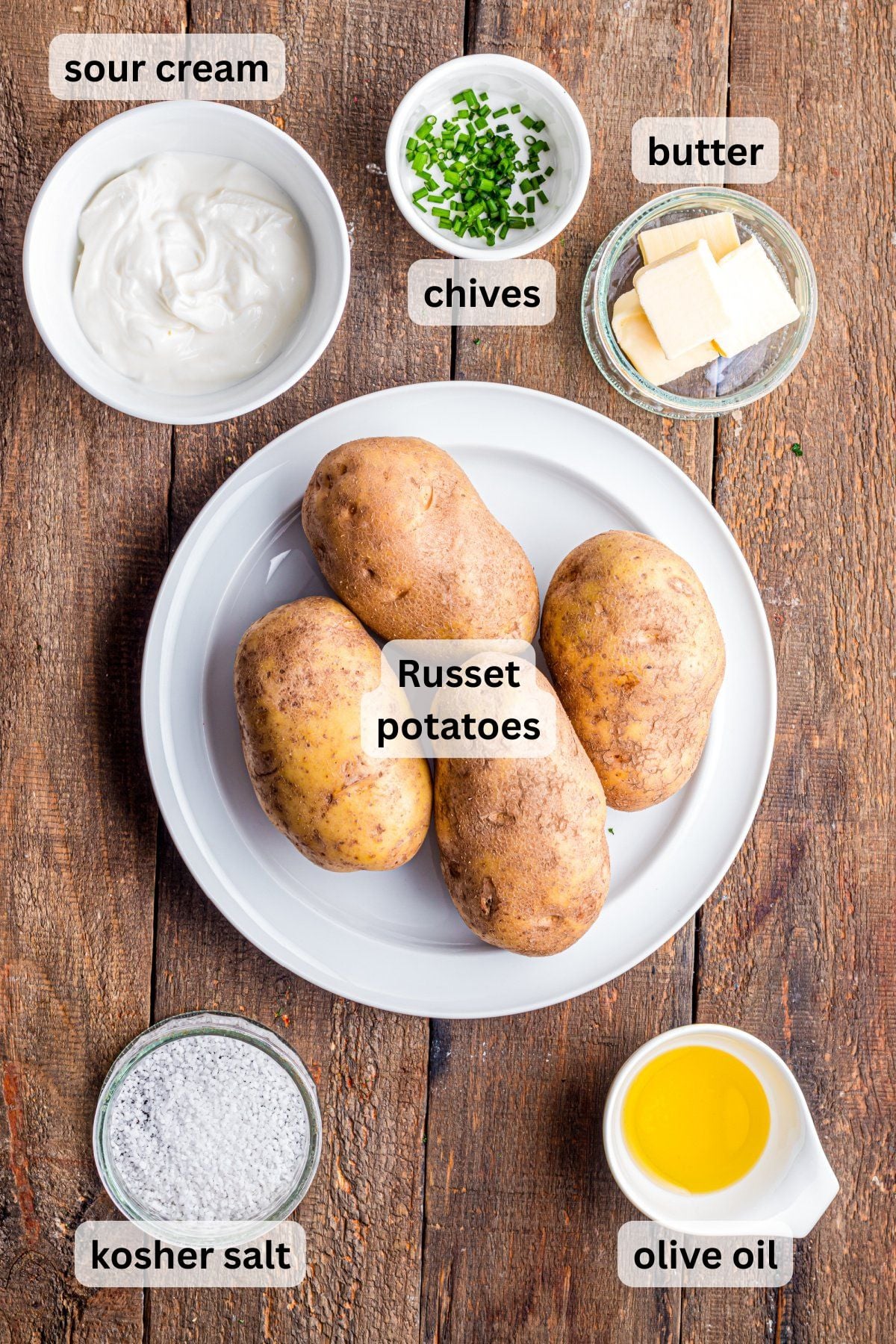 All of the ingredients needed to make a steakhouse-baked-potato on a table in bowls and a plate.