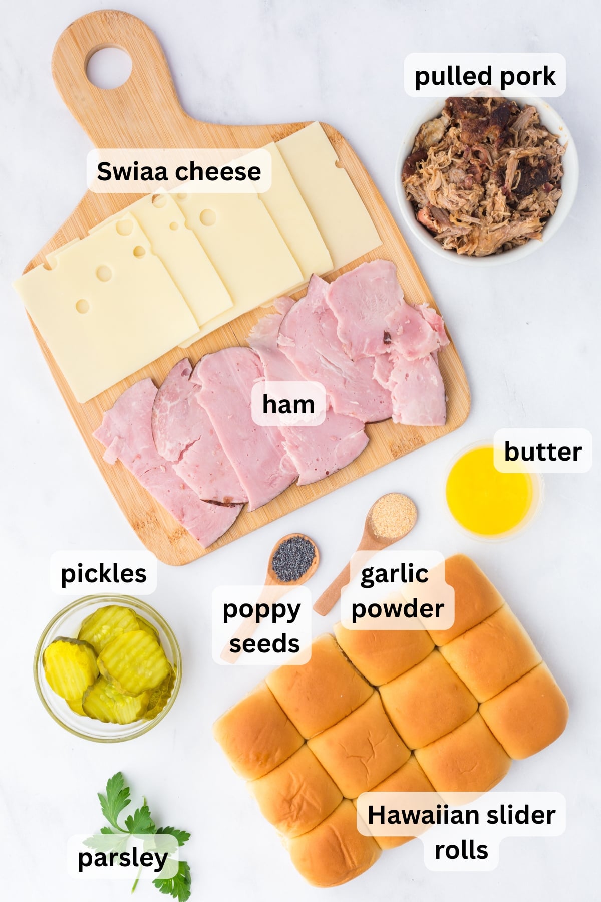 ingredients for cuban sliders including ham pulled pork swiss cheese pickles and rolls on a table.