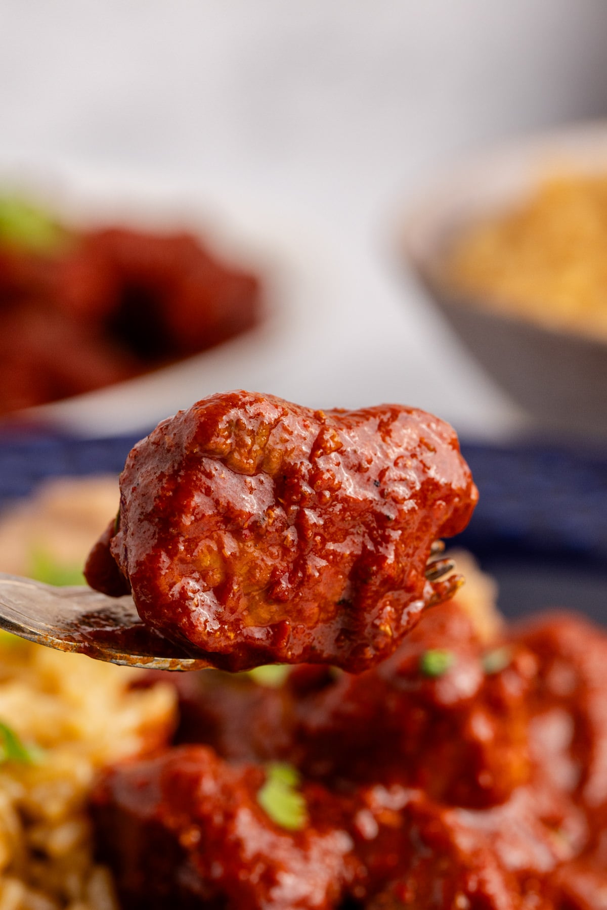 A fork holding up a piece of pork asado. 