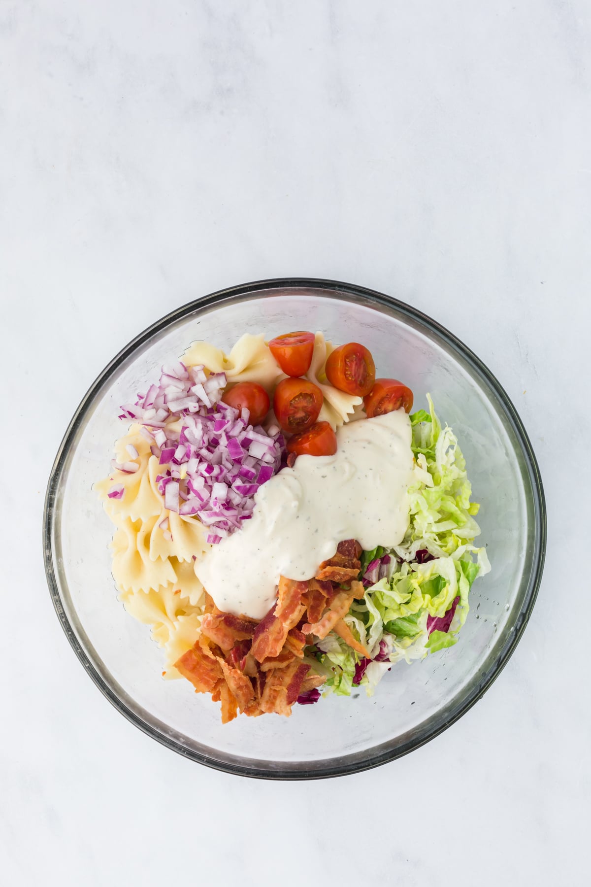 The pasta, cherry tomatoes, lettuce mix, bacon, red onion and dressing in a bowl