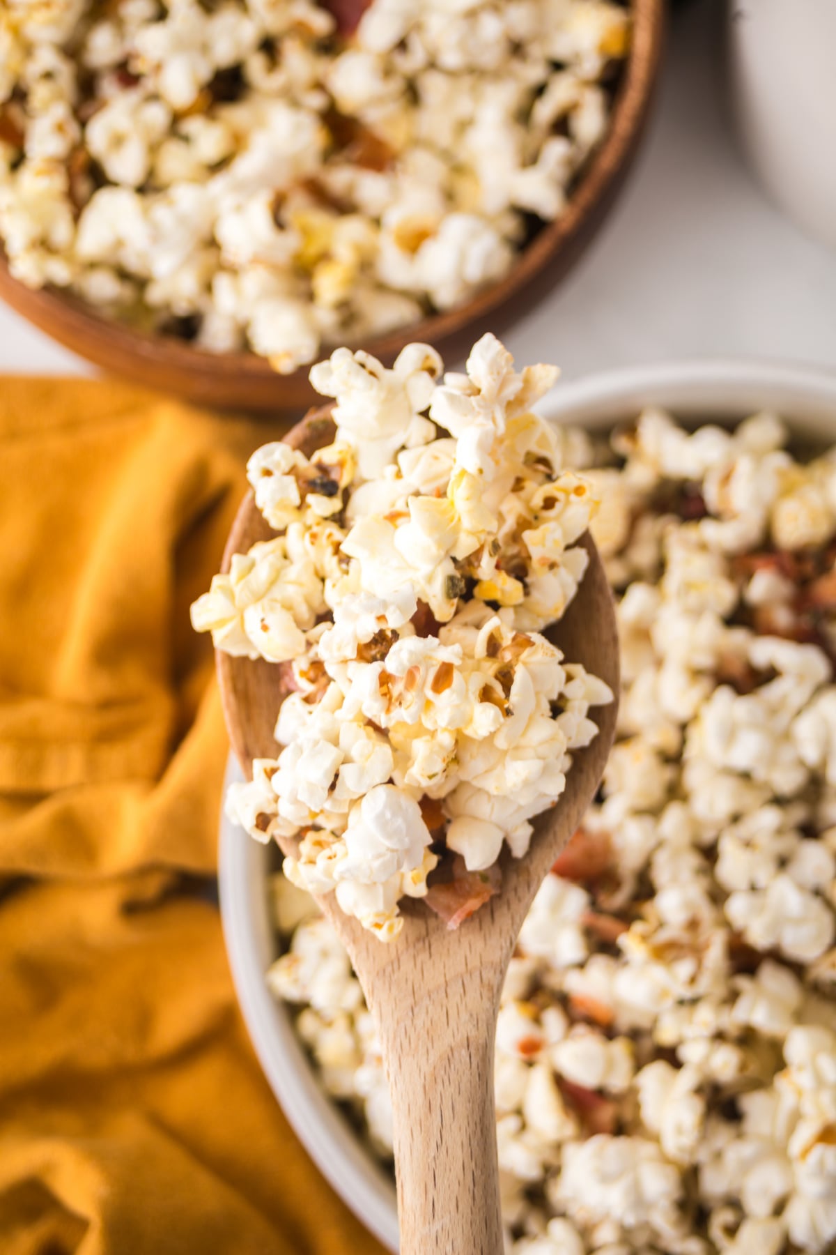 A spoon full of popcorn over a small bowl of popcorn that's  in front of a larger bowl of popcorn.