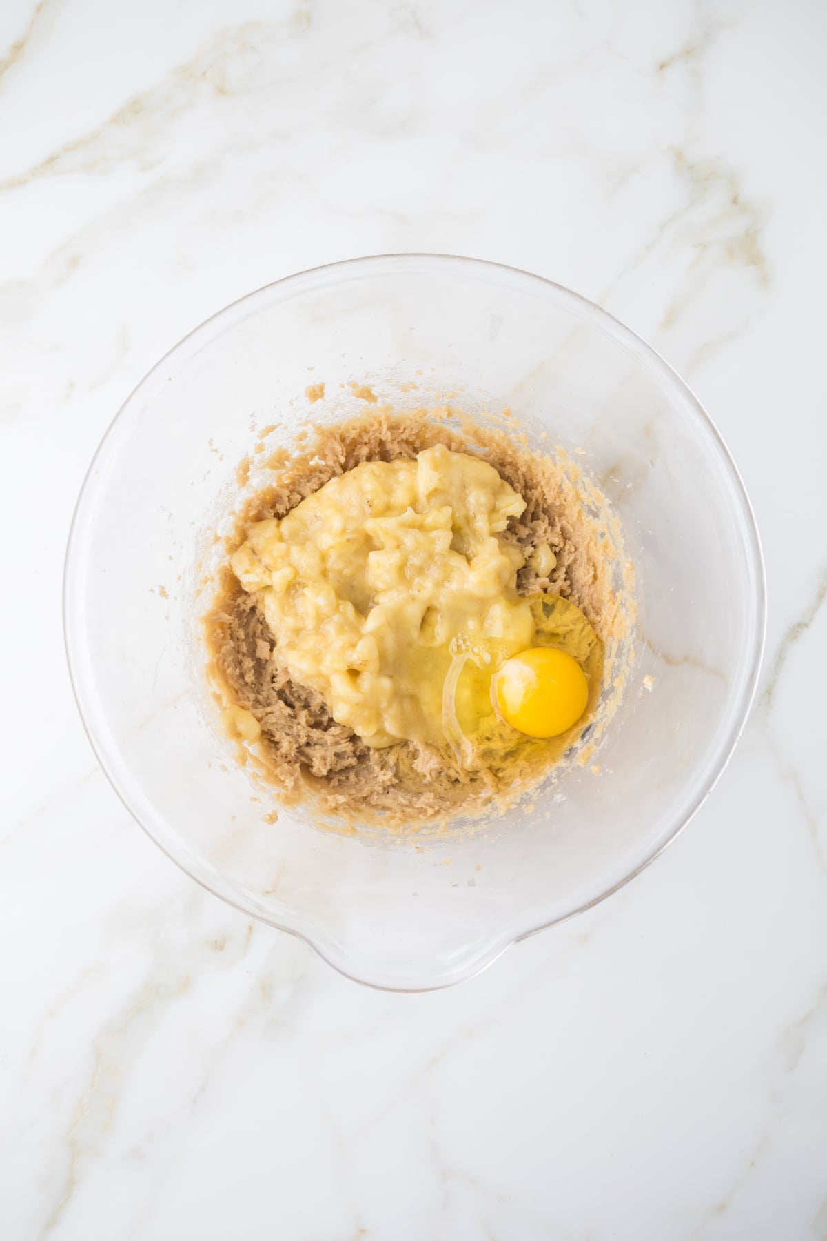 mixing banana bread cake batter with mashed bananas egg butter and sugar in bowl
