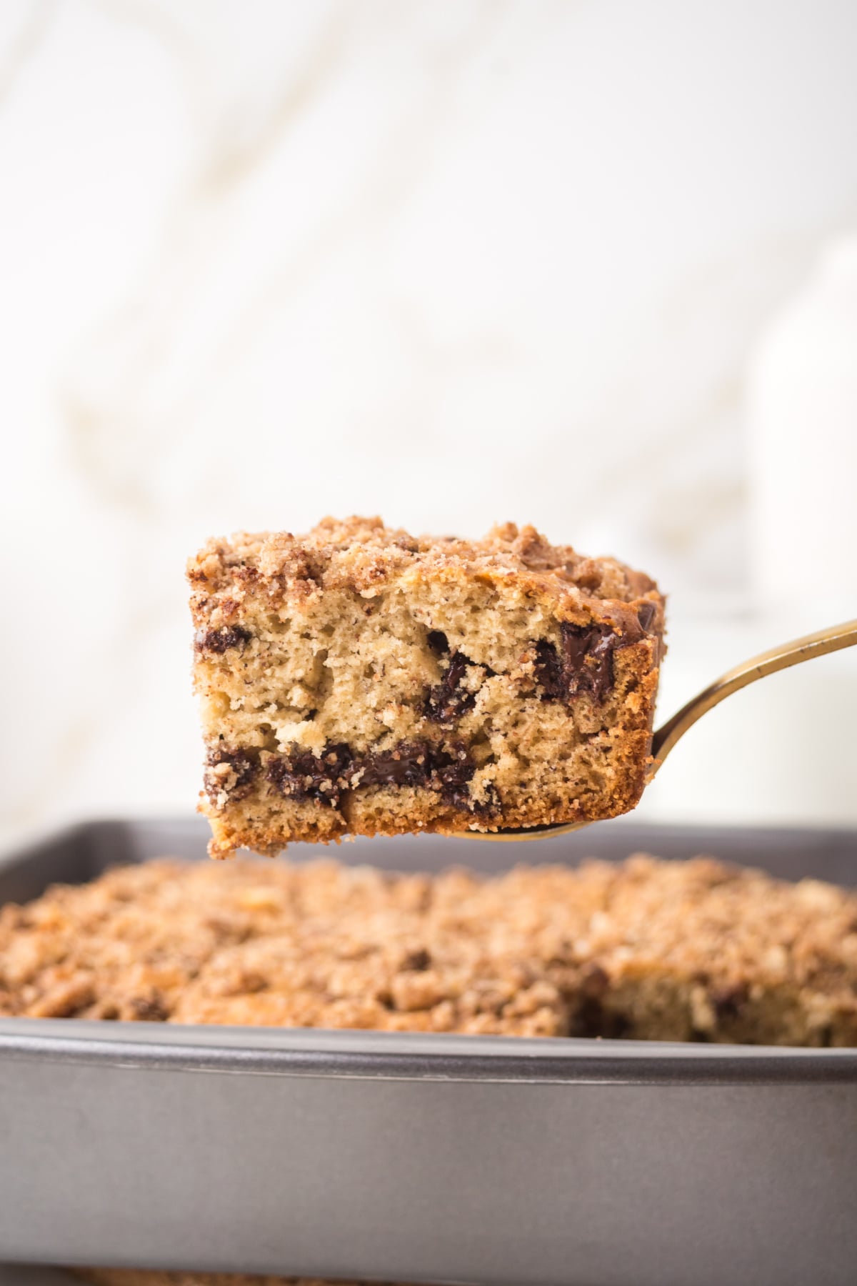 a slice of banana bread cake held in the air on a spatula showing soft moist texture with chocolate chips inside