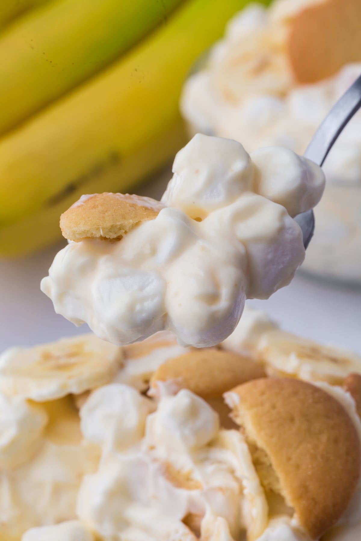A spoonful of banana pudding fluff dessert held in the air on top of a bowlful
