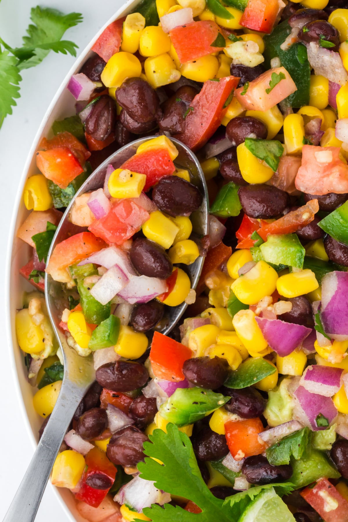 A spoonful of salad in the bowl full of salad on a table.