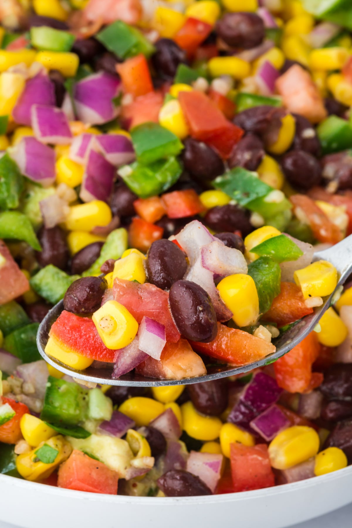 A spoonful of salad held in the air above a bowl full of salad.
