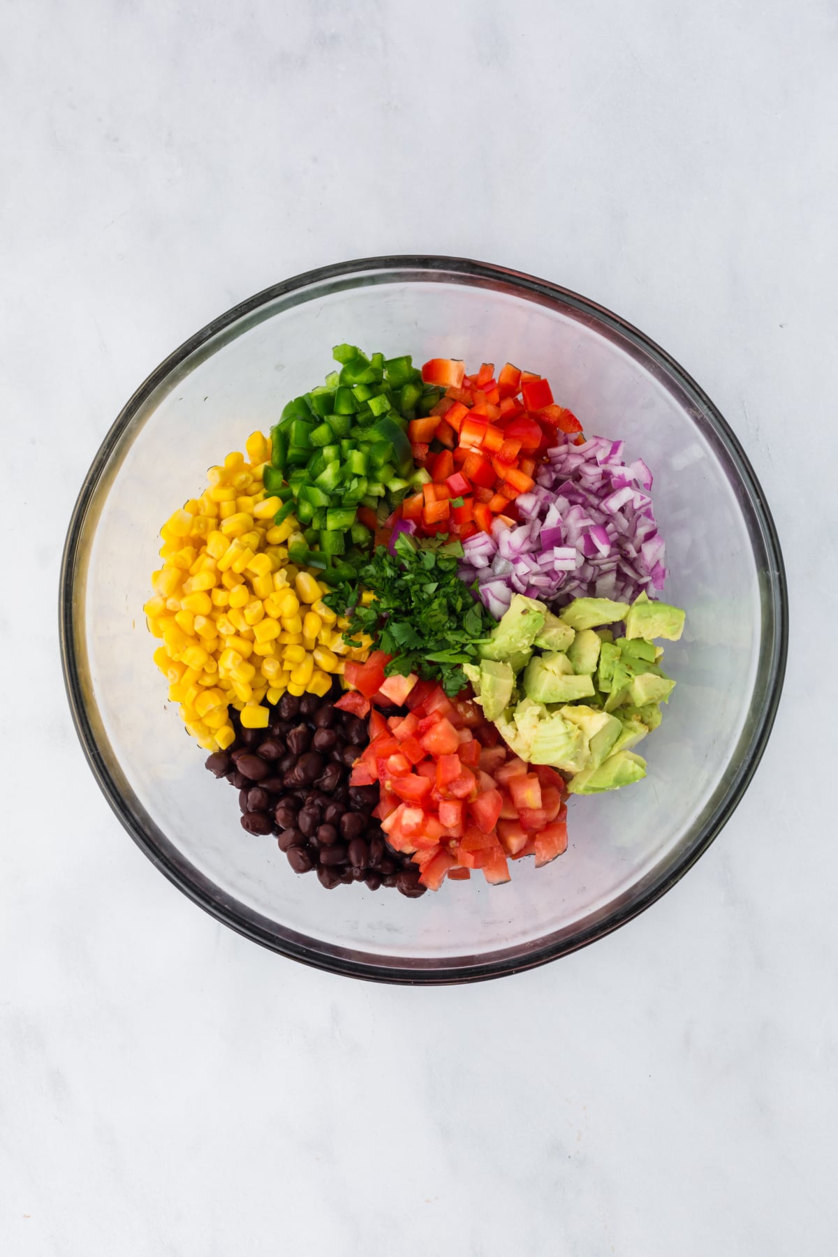 Black beans, sweet corn, avocado, red onion, tomato, red pepper, green pepper, and cilantro in a bowl on a table.