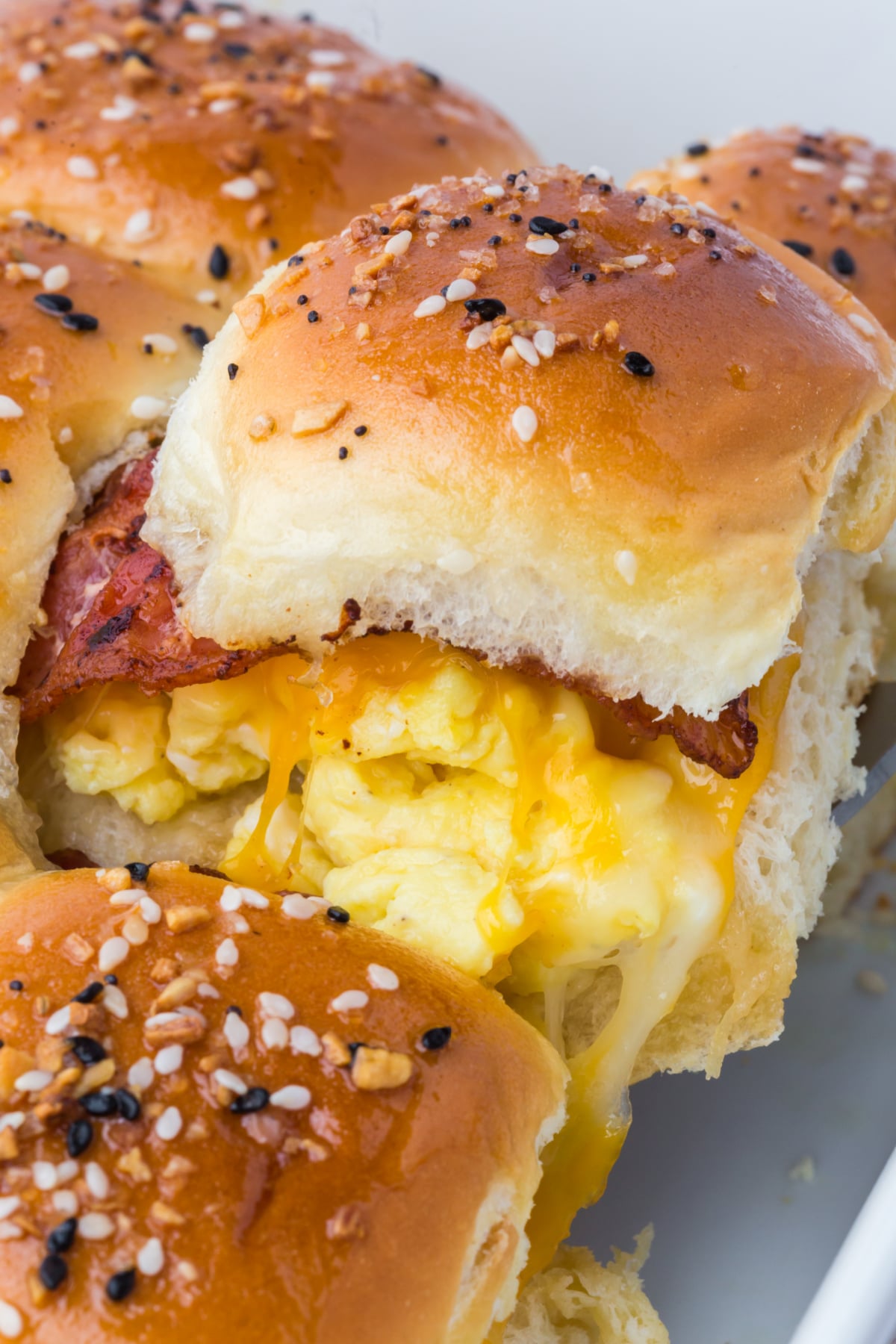 cheesy breakfast slider with melted cheese and bacon being lifted out of baking dish