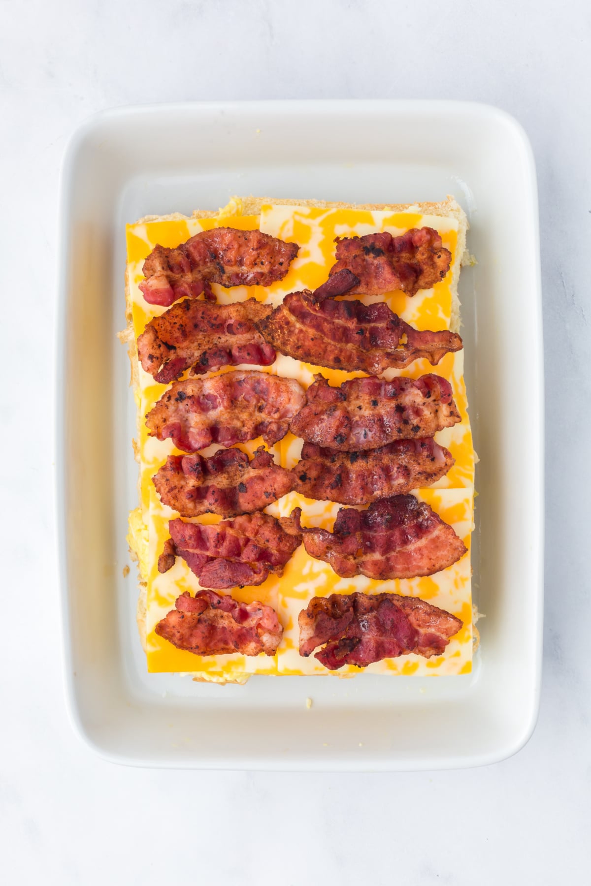 layering cheese eggs and bacon on slider buns in baking dish