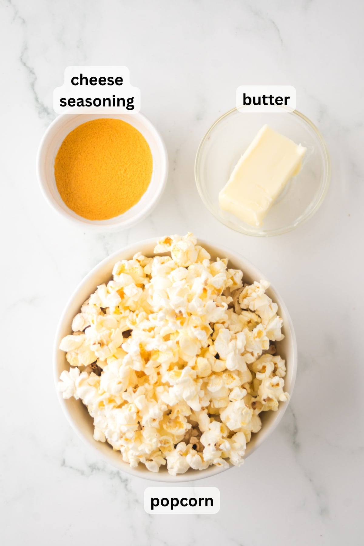 All of the ingredients needed to make cheddar cheese popcorn in bowls on a table.