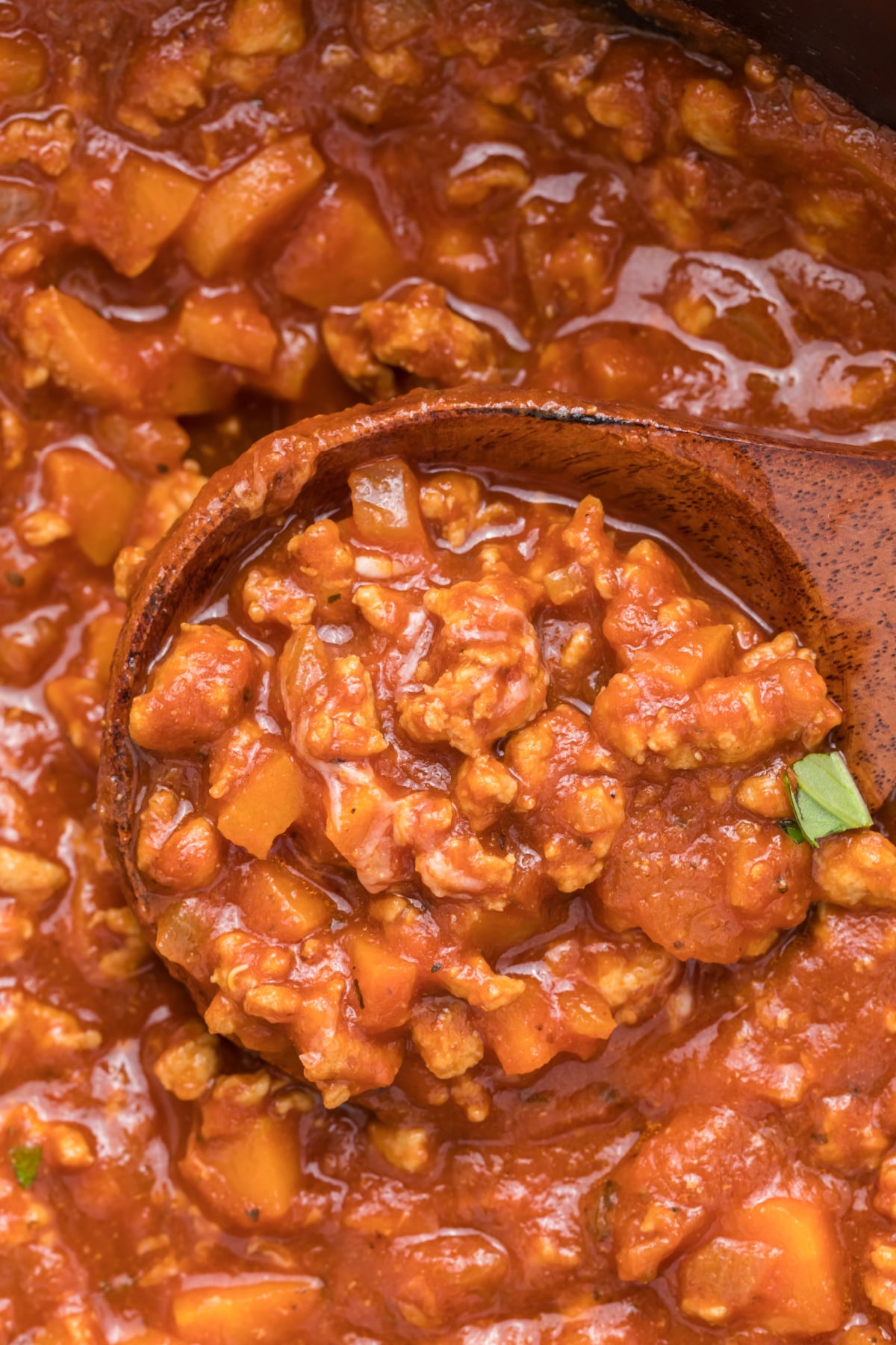 A wooden spoon is scooping up some chicken bolognese.