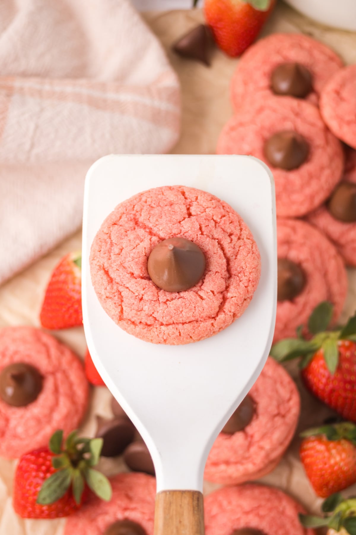 strawberry cookies with hershey kisses on spatula held above cookies on parchment 