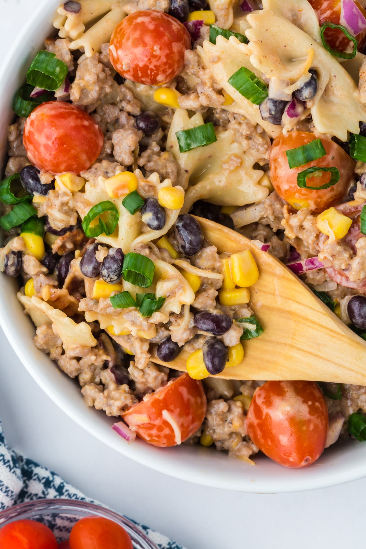 wooden spoonful inside bowl of cowboy pasta salad showing sausage bacon and creamy dressing on table