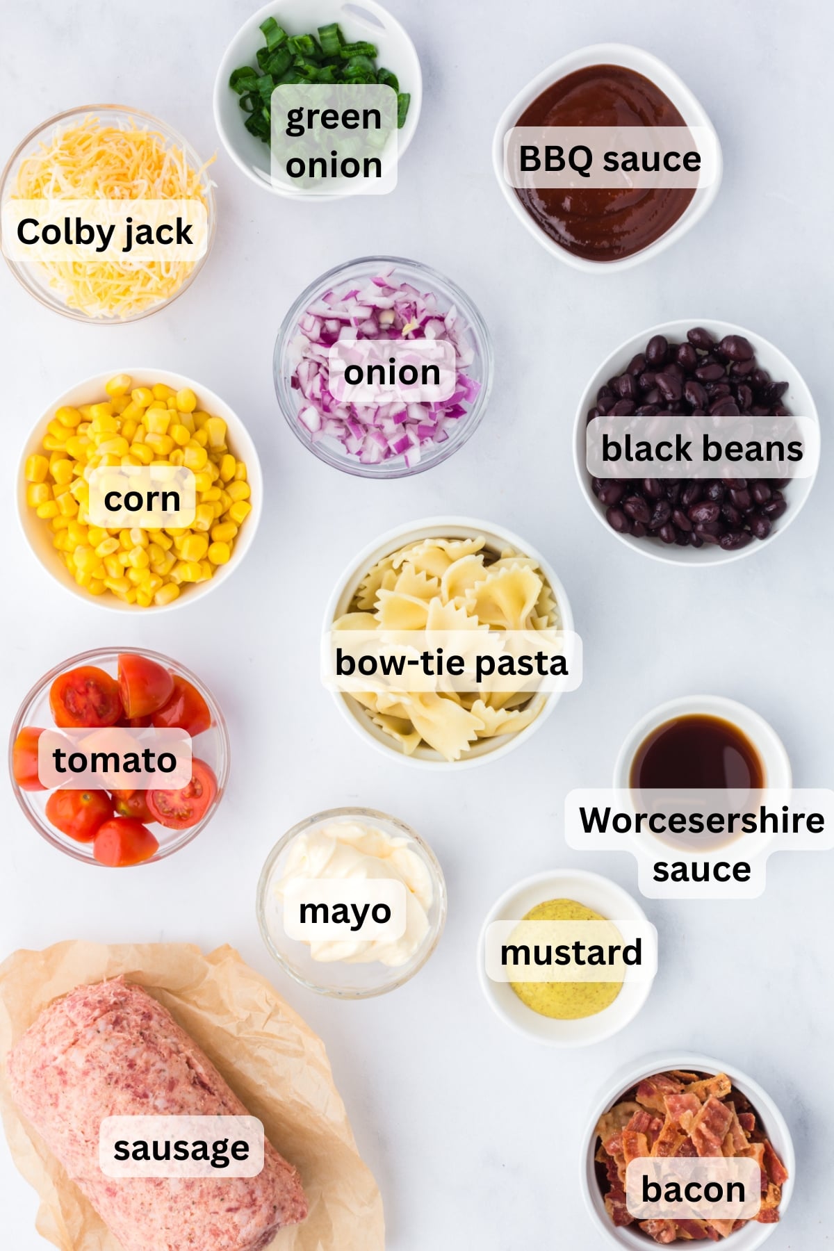 ingredients for cowboy pasta salad including pasta sausage bacon corn beans and dressing in bowls on table