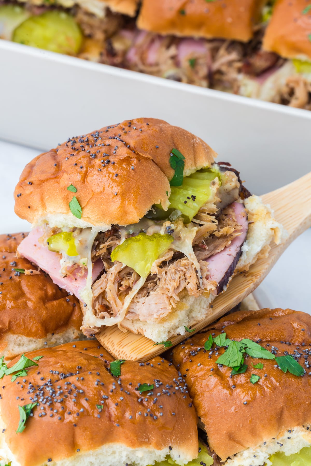 A cuban slider showing layers of ham pork cheese and pickles while being lifted out of casserole dish