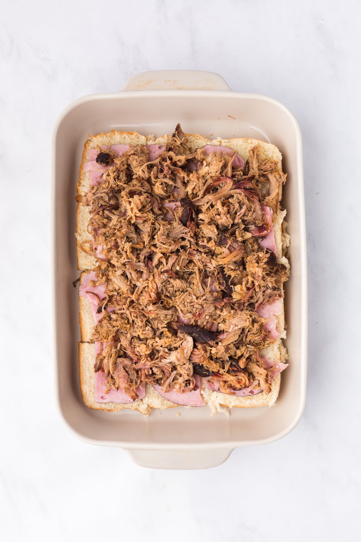 layering ham and pulled pork on slider rolls for cuban sliders