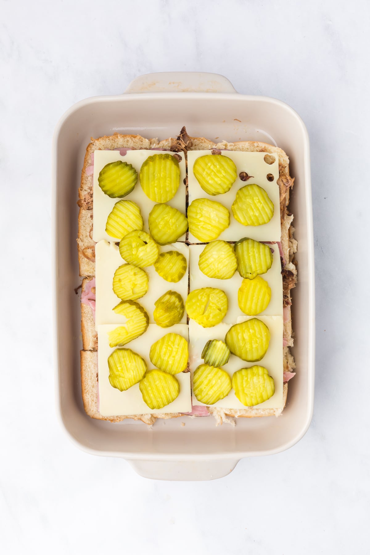 adding swiss cheese and pickles to cuban sliders