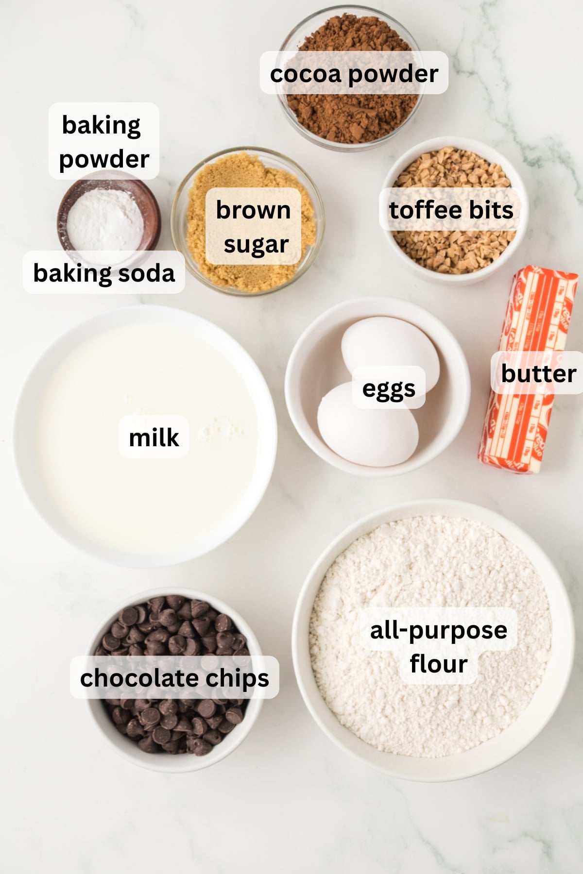 Ingredients for double chocolate chip muffins including cocoa powder, flour, eggs, milk, butter, and chocolate chips in bowls on a table