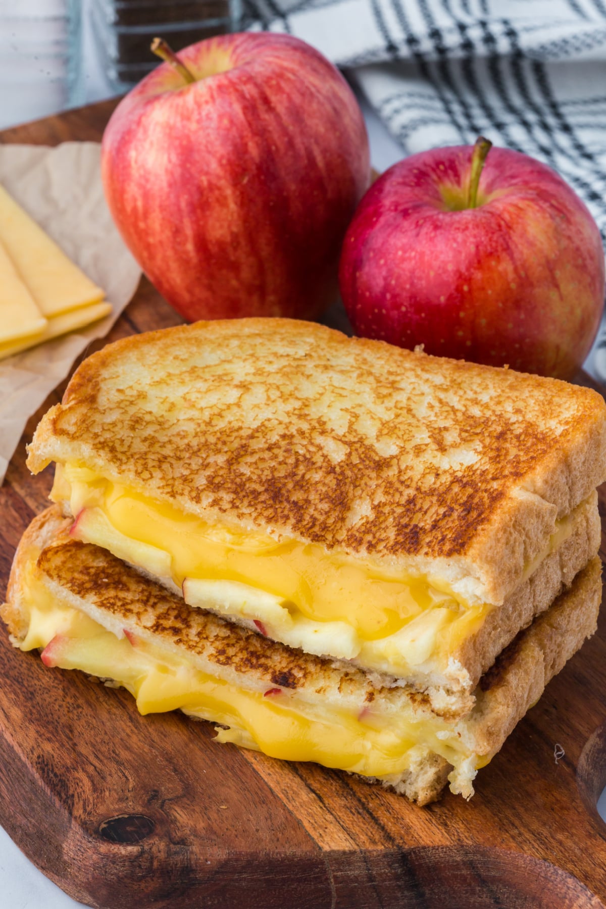 grilled cheese sandwich with two halves on top of each other showing melted cheese and apple slices inside on cutting board