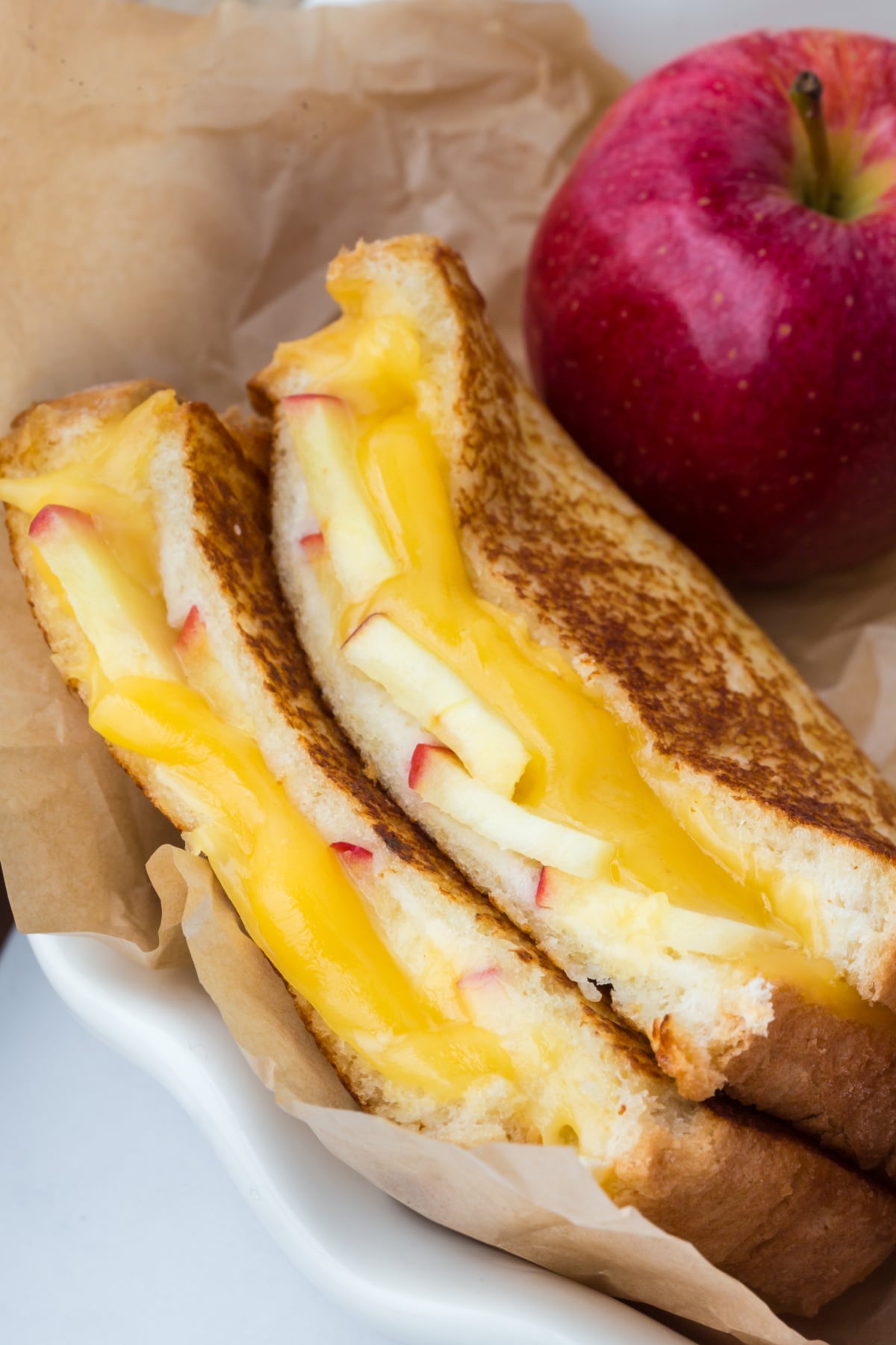 grilled cheese sandwich sliced in half with halves on top of each other on parchment covered plate with apple