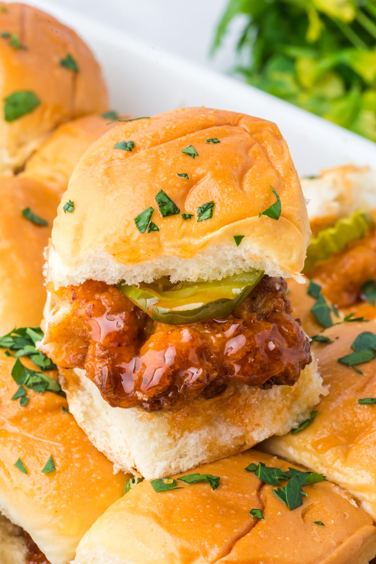 a hot honey chicken slider on  top of others showing crispy chicken, pickle and sauce