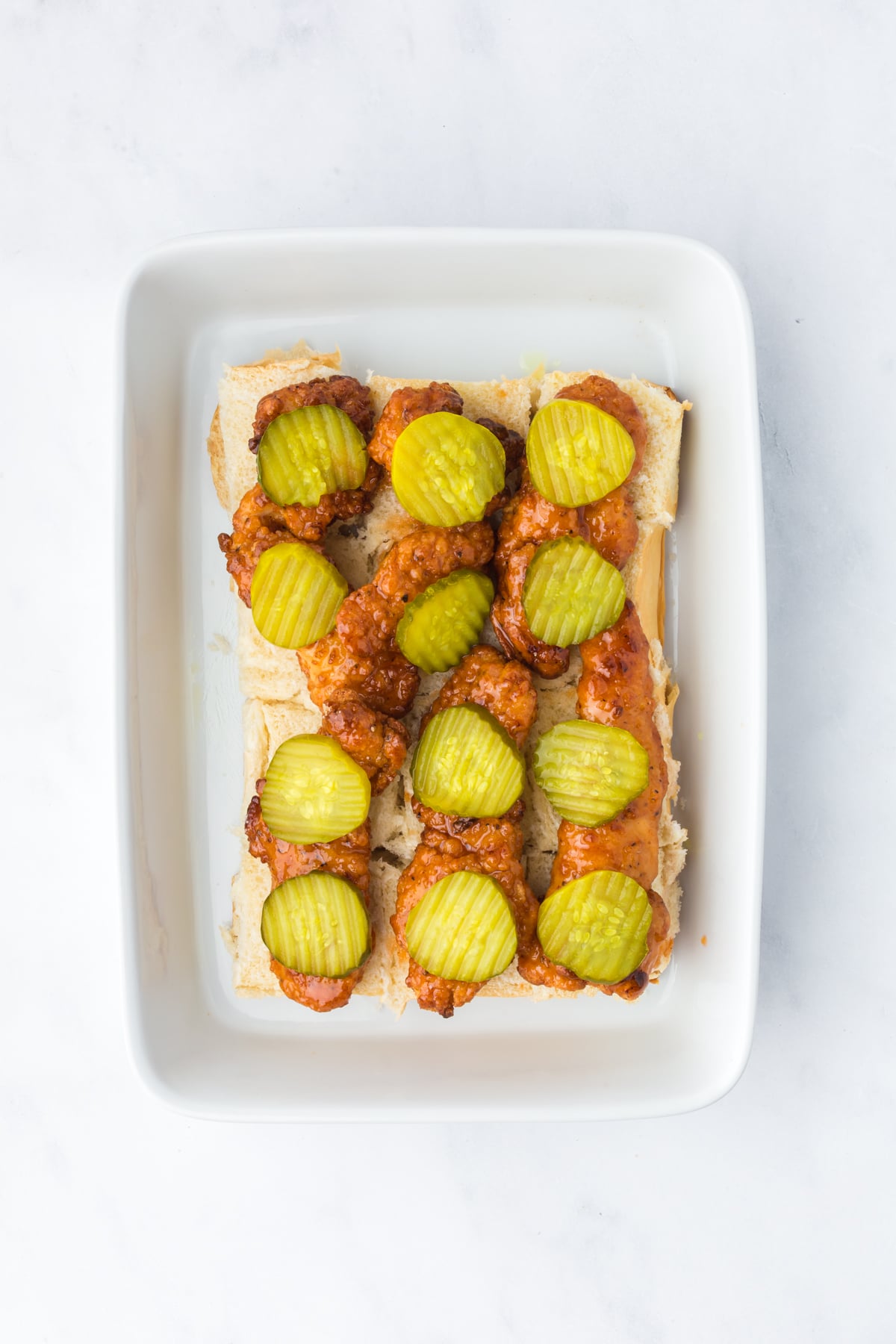 assembling hot honey chicken sliders with chicken tenders and pickles on buns