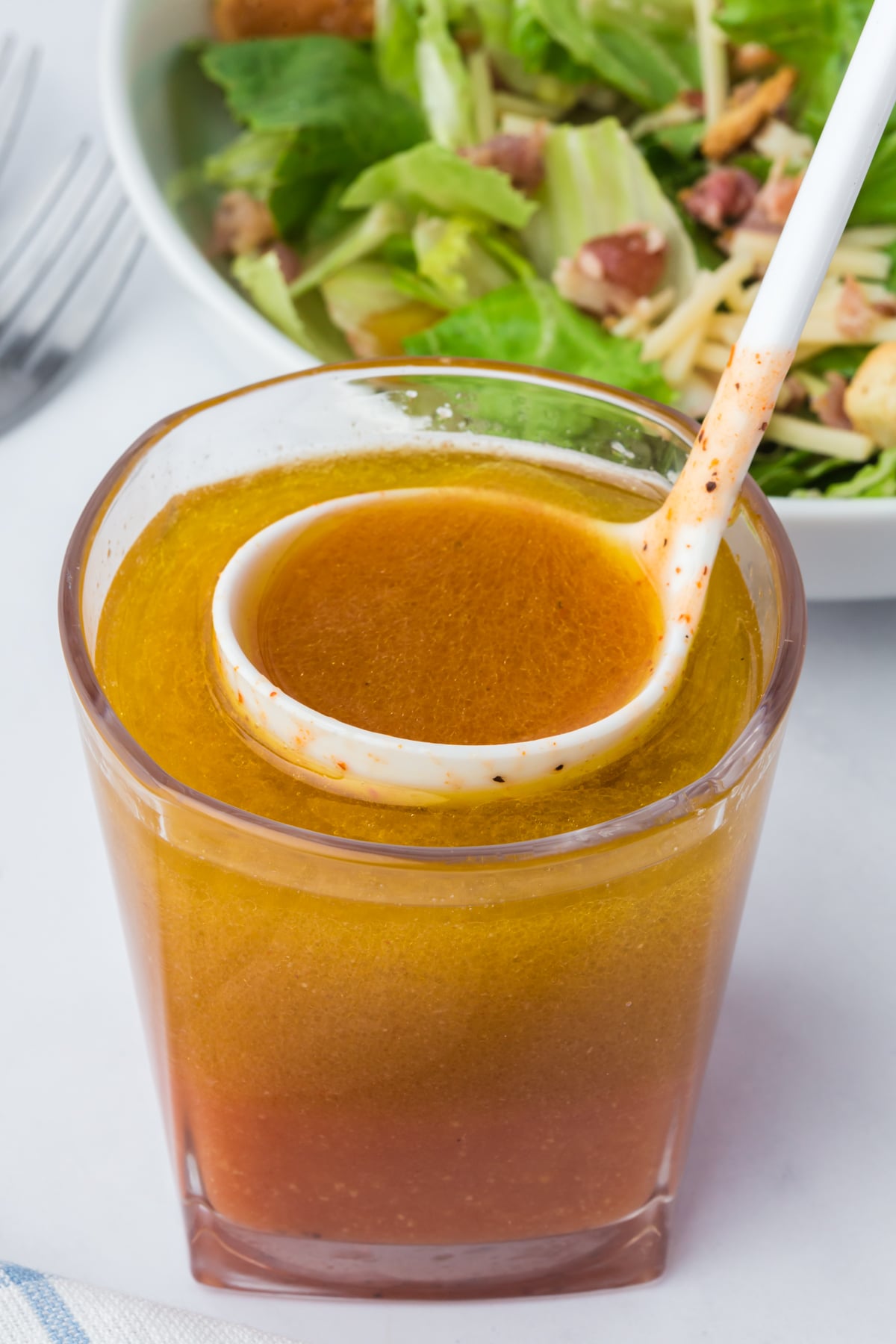 A ladle full of vinaigrette about to be lifted into the air and put on salad