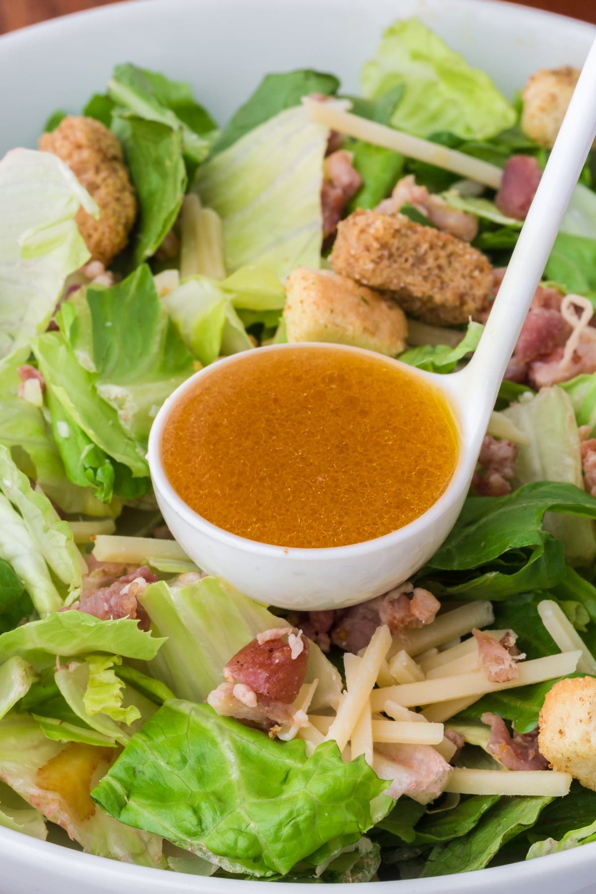 A full ladle about to pour vinaigrette over salad