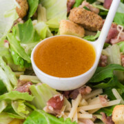 A full ladle about to pour hot honey vinaigrette over salad