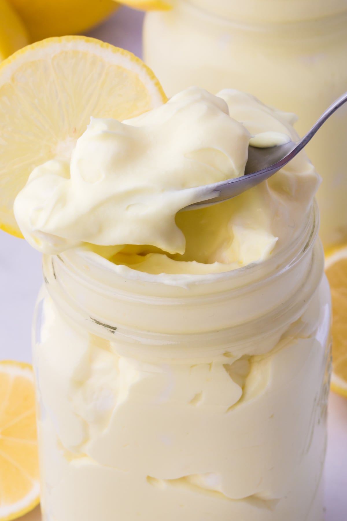 creamy lemon fluff dessert in mason jar topped with marshmallows and lemon slices with a spoonful being removed