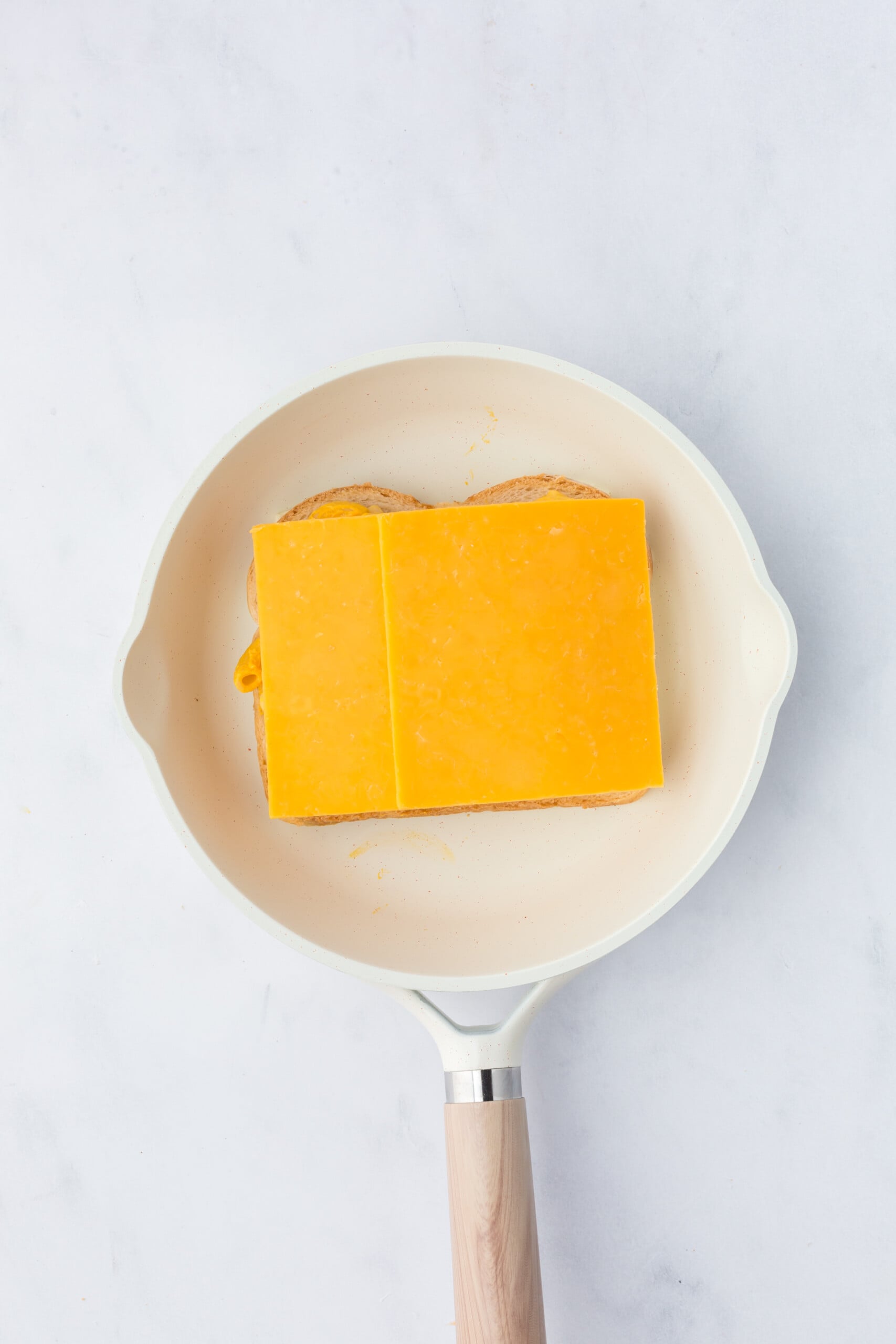 A slice of bread on a skillet topped with cheese, mac n cheese and another slice of cheese