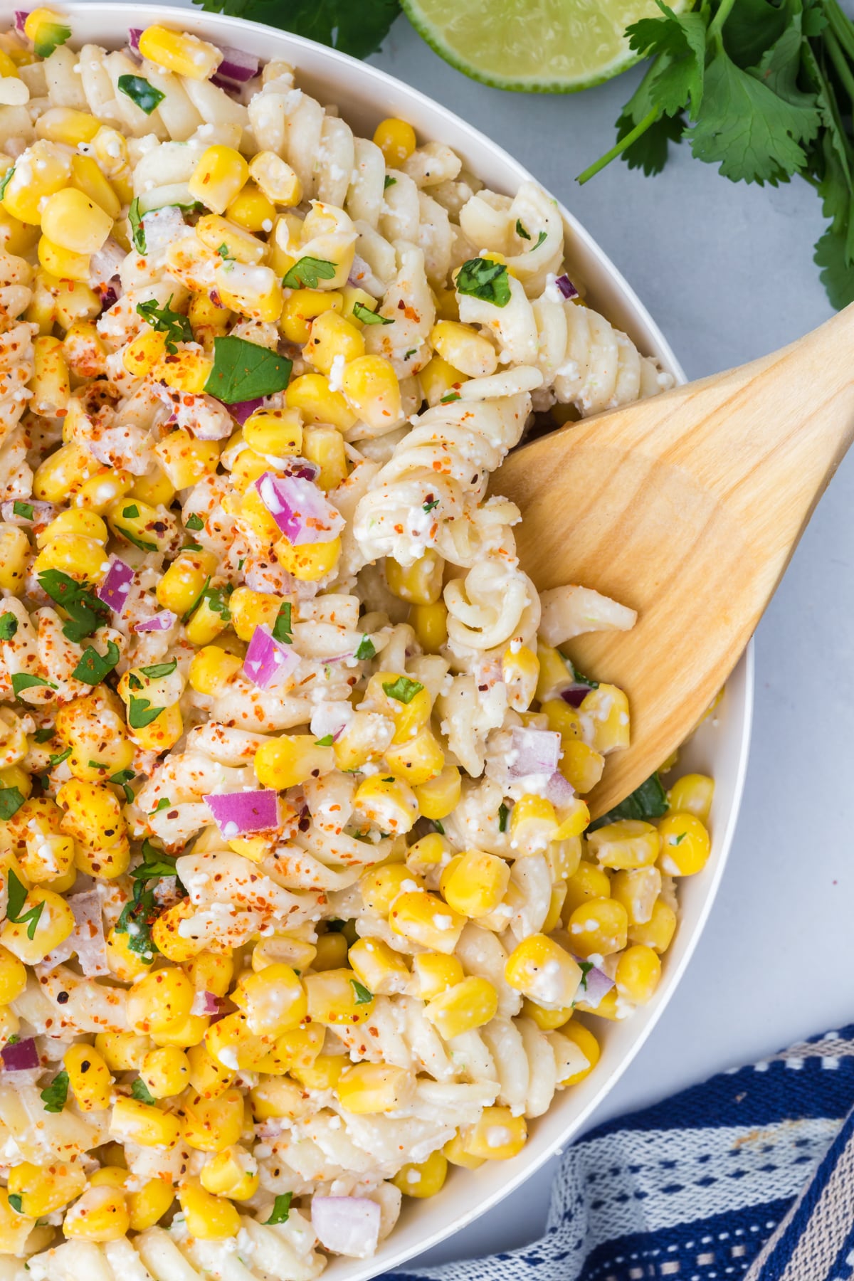 creamy elote pasta salad with cotija cheese and corn on wooden spoon in bowl