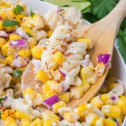 a wooden spoonful of mexican street corn pasta salad lifting in bowl with creamy dressing cotija cheese and lime