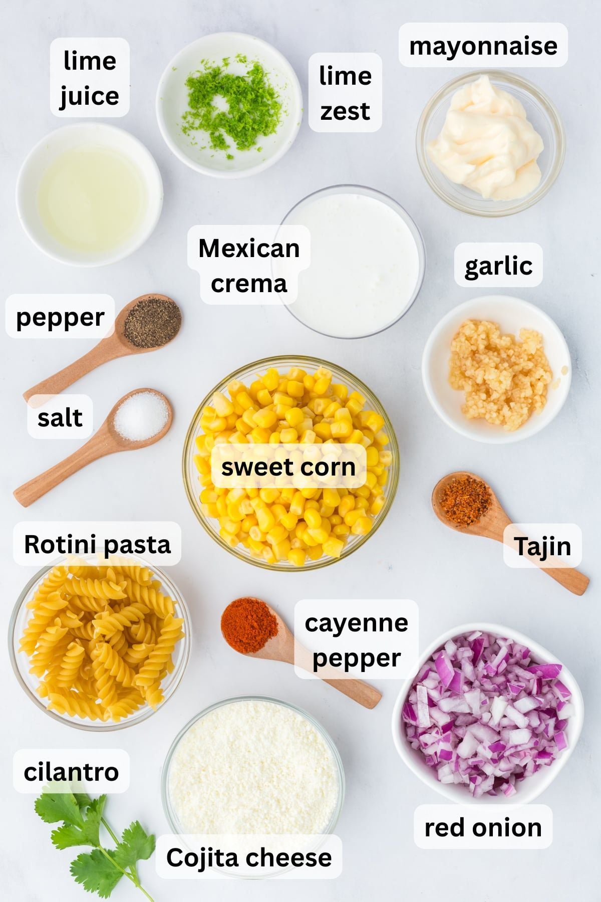 All the ingredients needed to make Mexican Street Corn Pasta including pasta corn lime cotija cheese and crema in bowls on a table