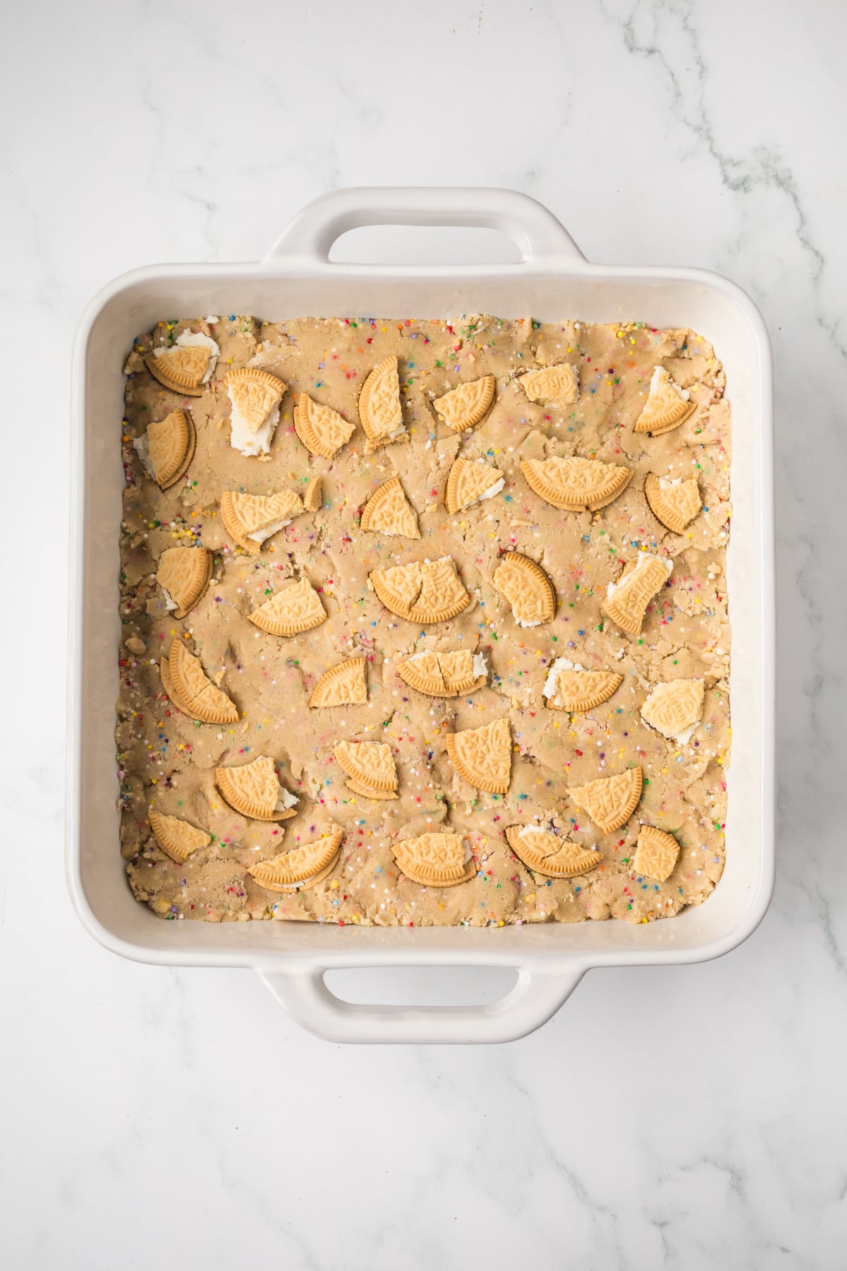 oreo cookie dough pressed into baking pan with chopped oreos on top