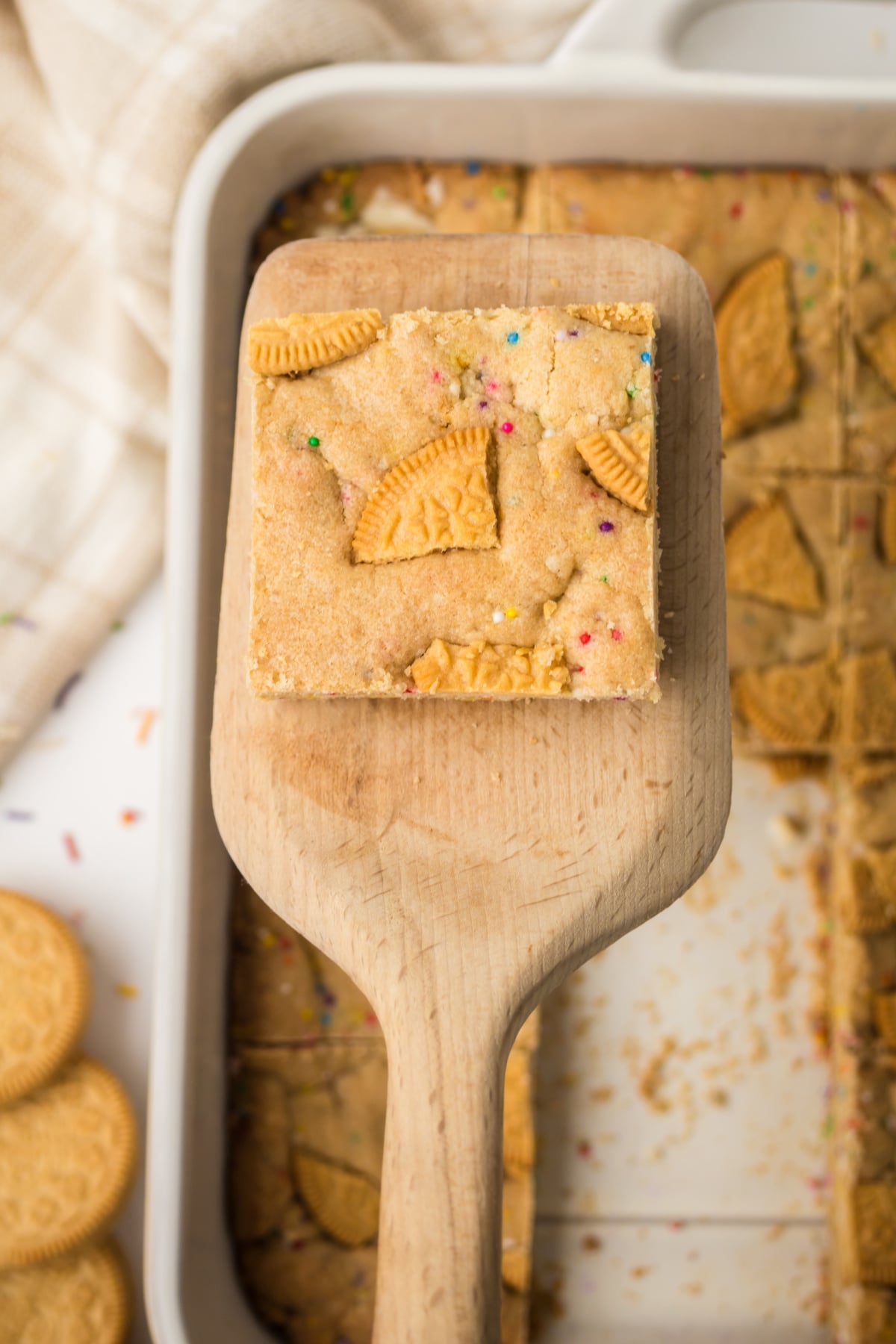 soft chewy oreo cookie bar with cookies and cream texture on spatula lifted in air above pan.
