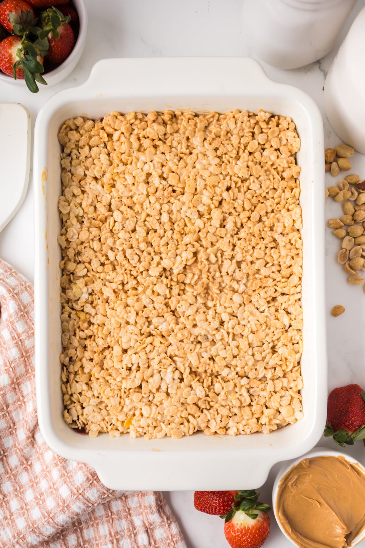 layering peanut butter rice krispie mixture with strawberry jelly in baking dish