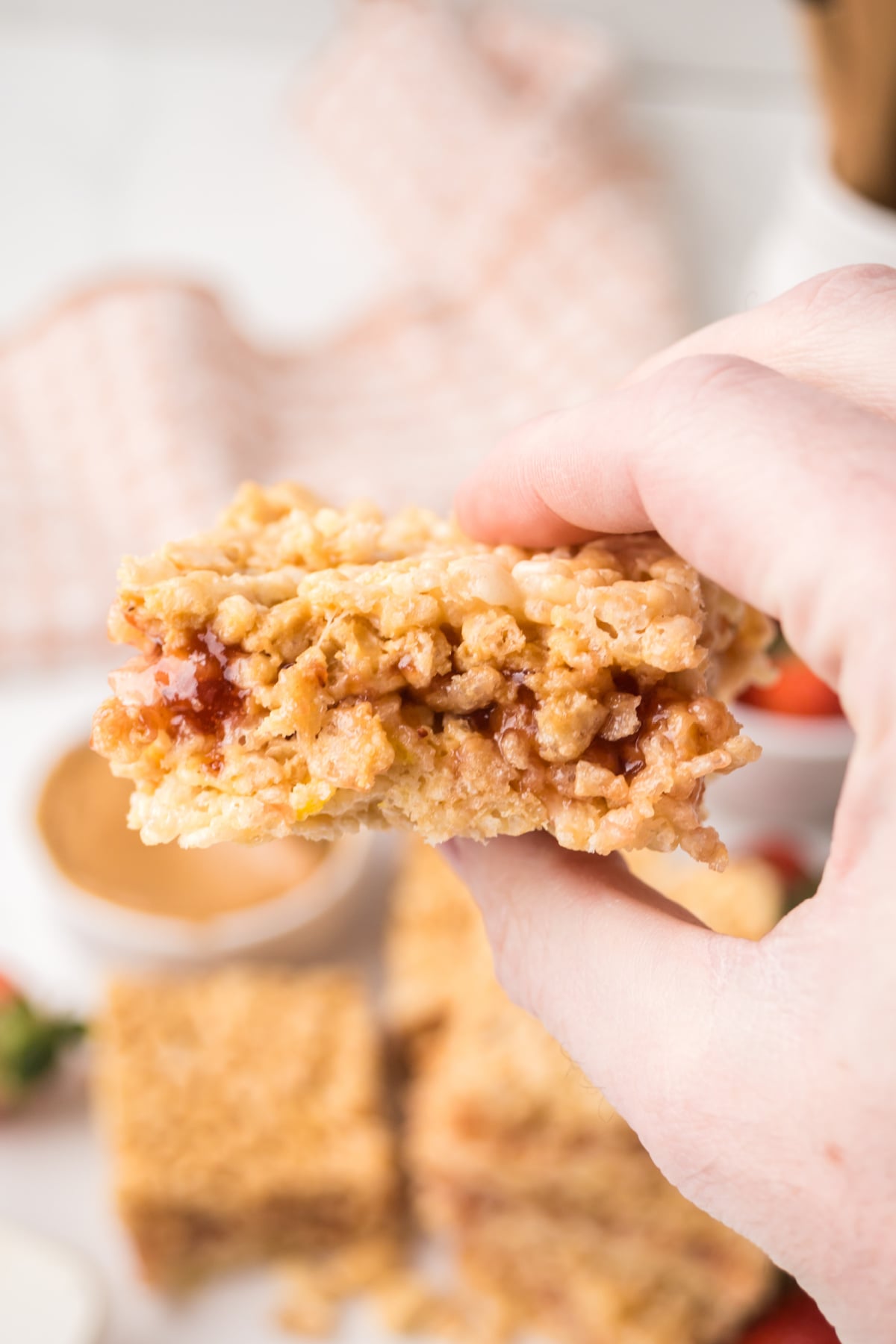 homemade peanut butter jelly rice krispie treat showing jelly layer with square held in air 