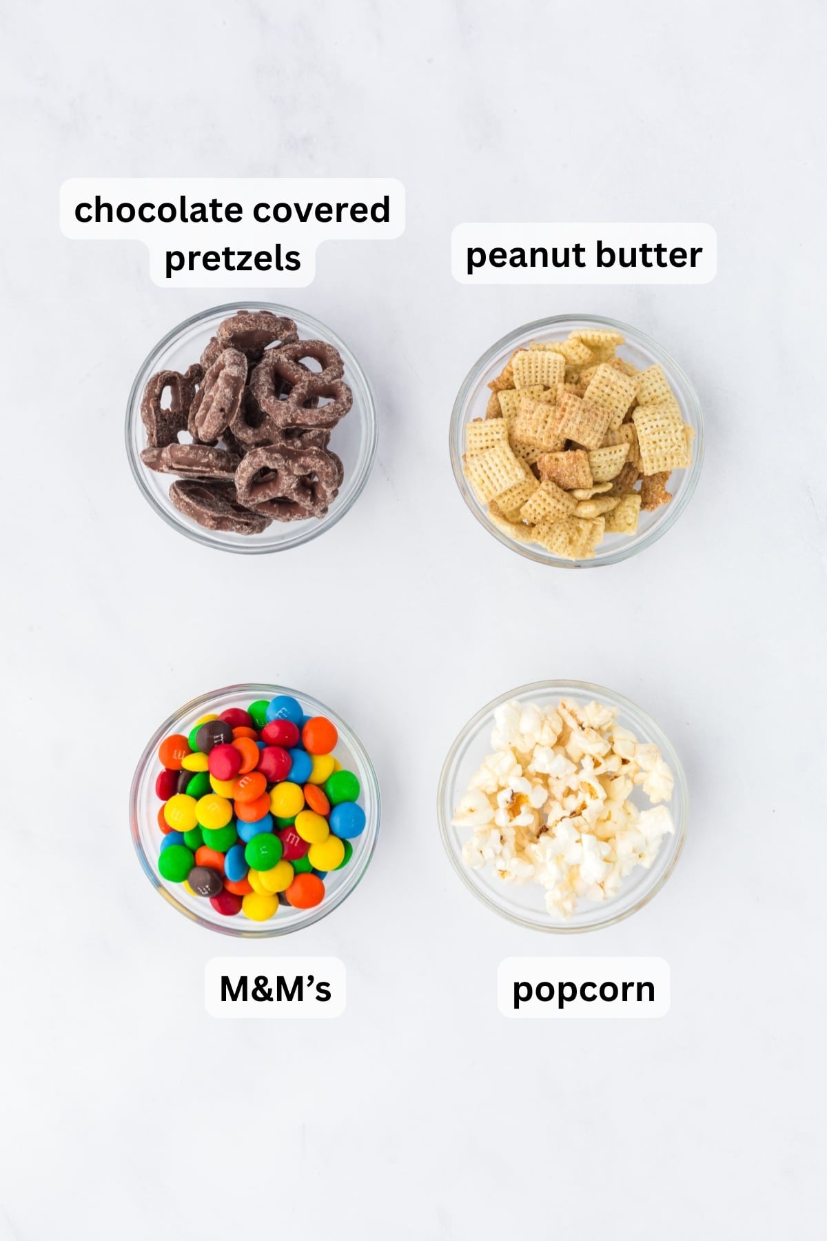ingredients for popcorn trail mix including popcorn cereal m&ms and chocolate covered pretzels in bowls on a table