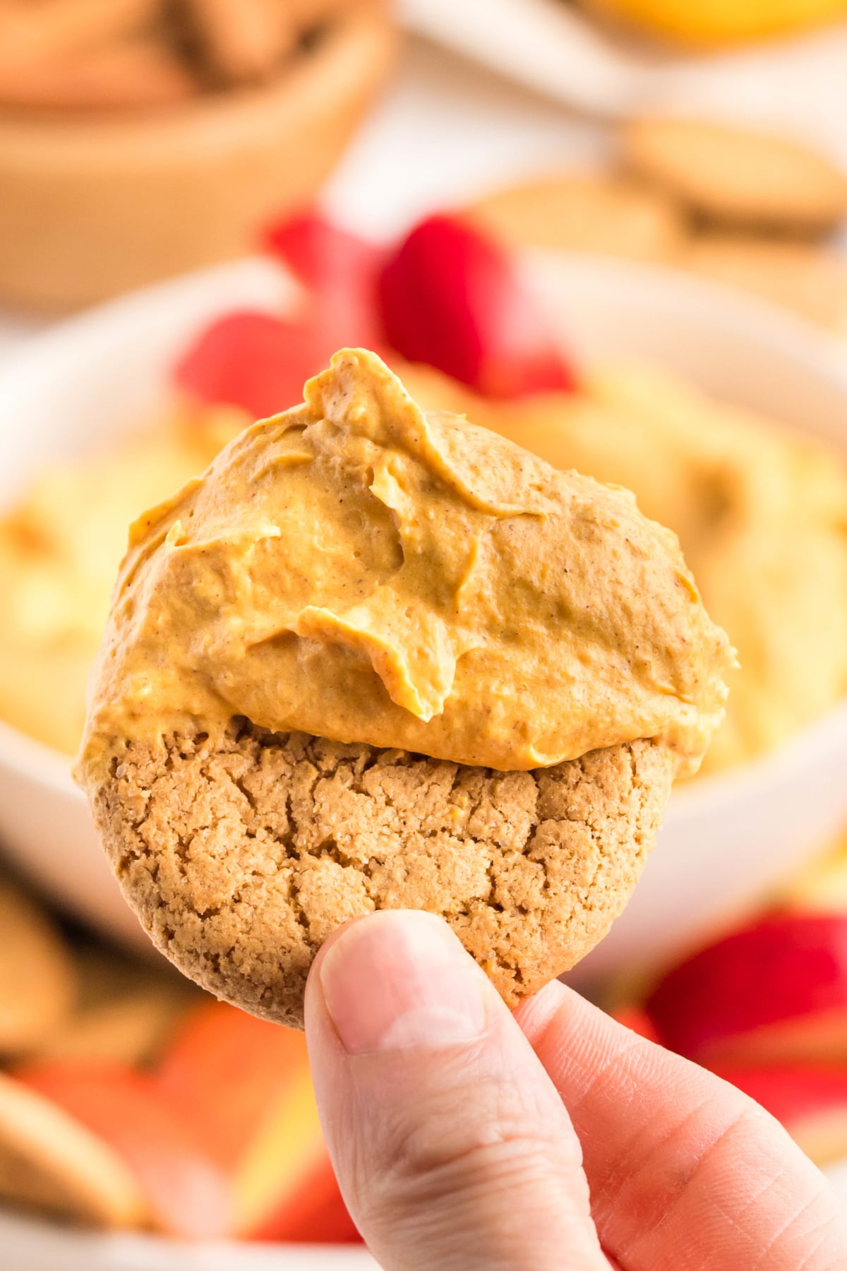 A cookie dipped into the pumpkin fluff and being held up in the air.